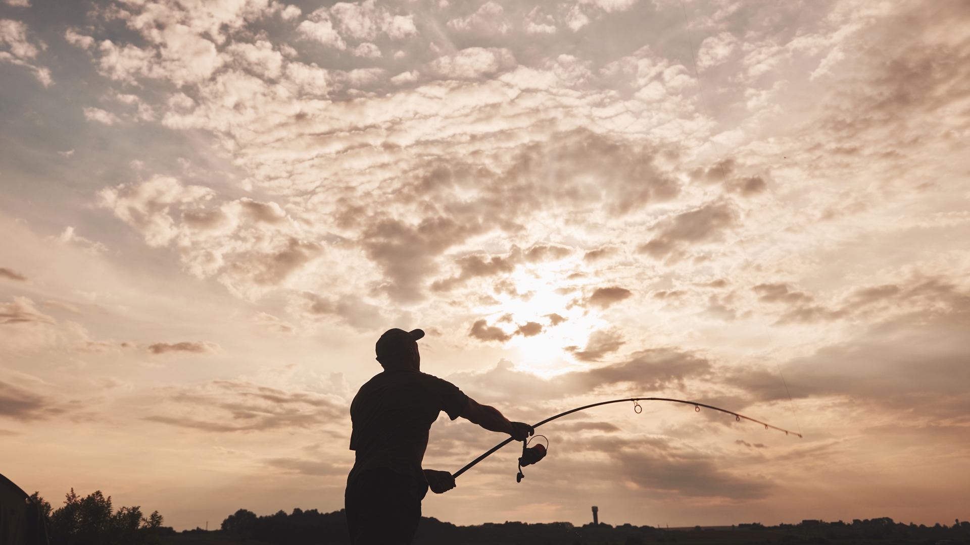 Silhouette of fisherman throws a fishing pole into the lake at sunset